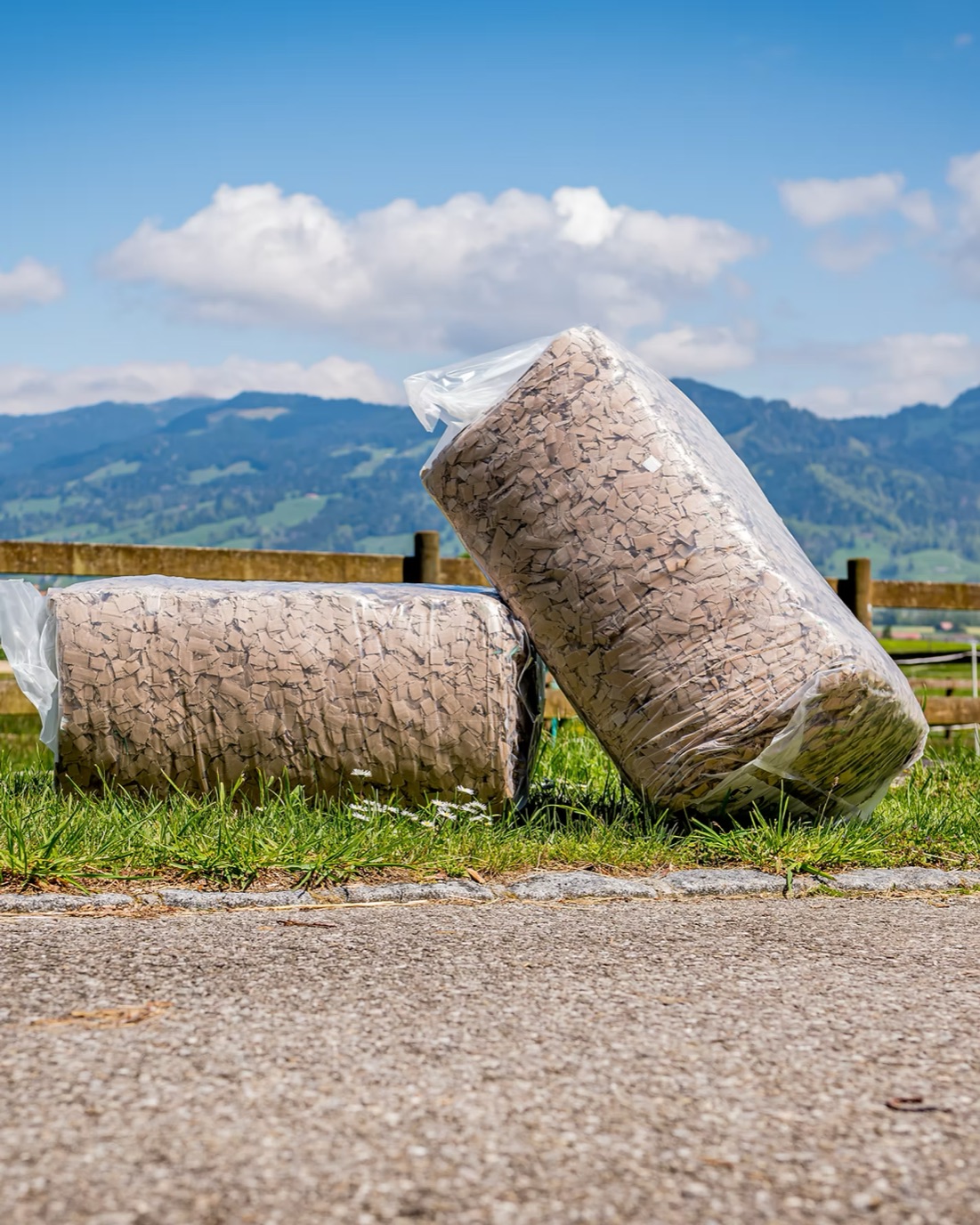 Deux sacs de litière Hippelia posés dans l’herbe, devant une clôture et des montagnes
